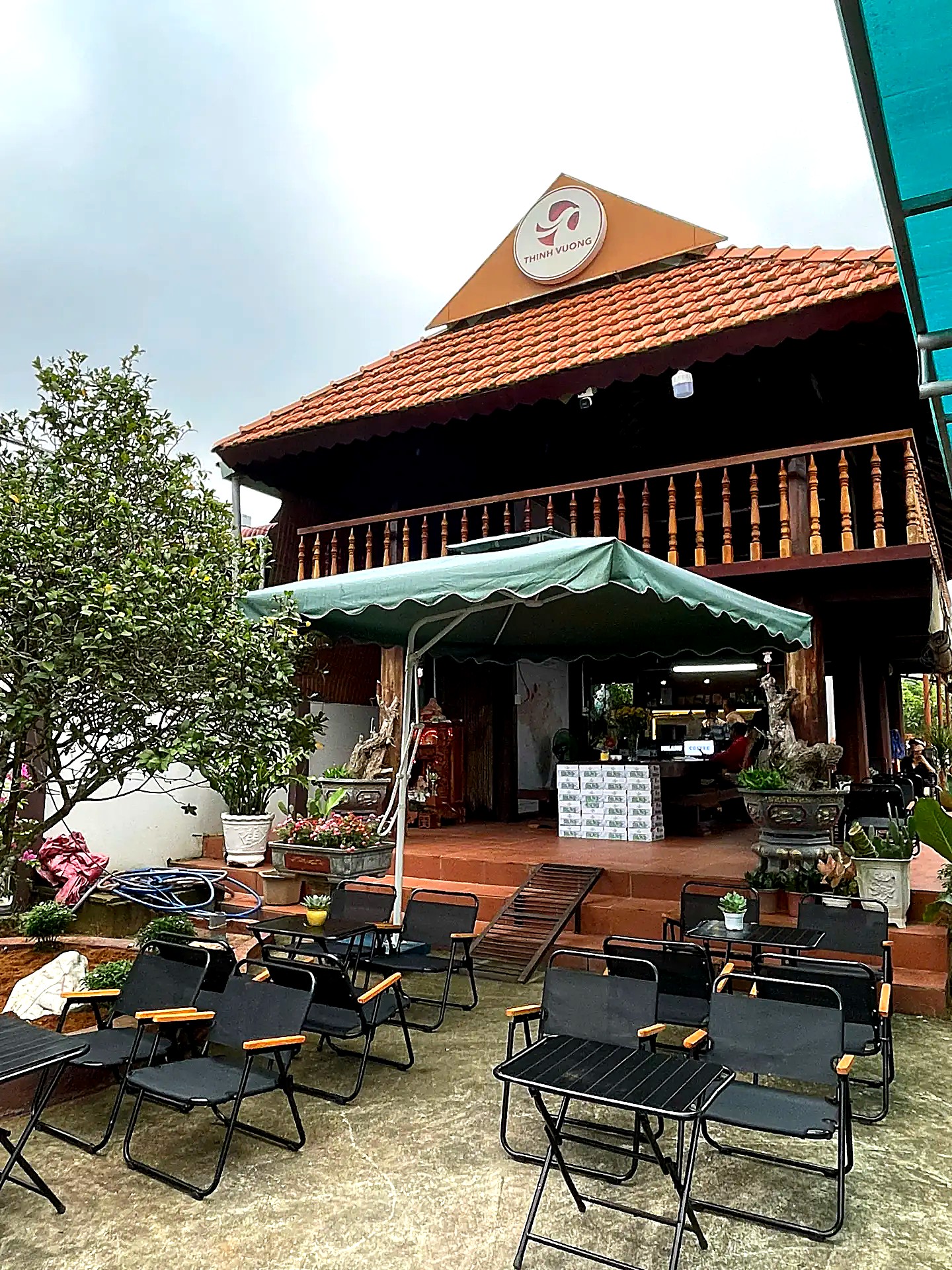 Nhà gỗ mái ngói Milano Coffee nhìn từ sân trước với dù xanh và bàn ghế