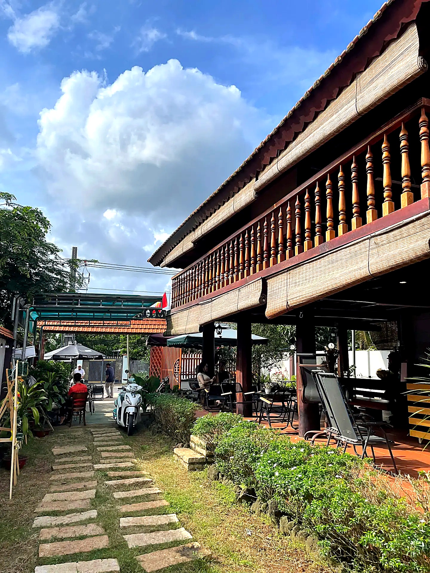 Nhà gỗ mái ngói Milano Coffee dưới trời xanh, lối đi lát đá qua sân vườn
